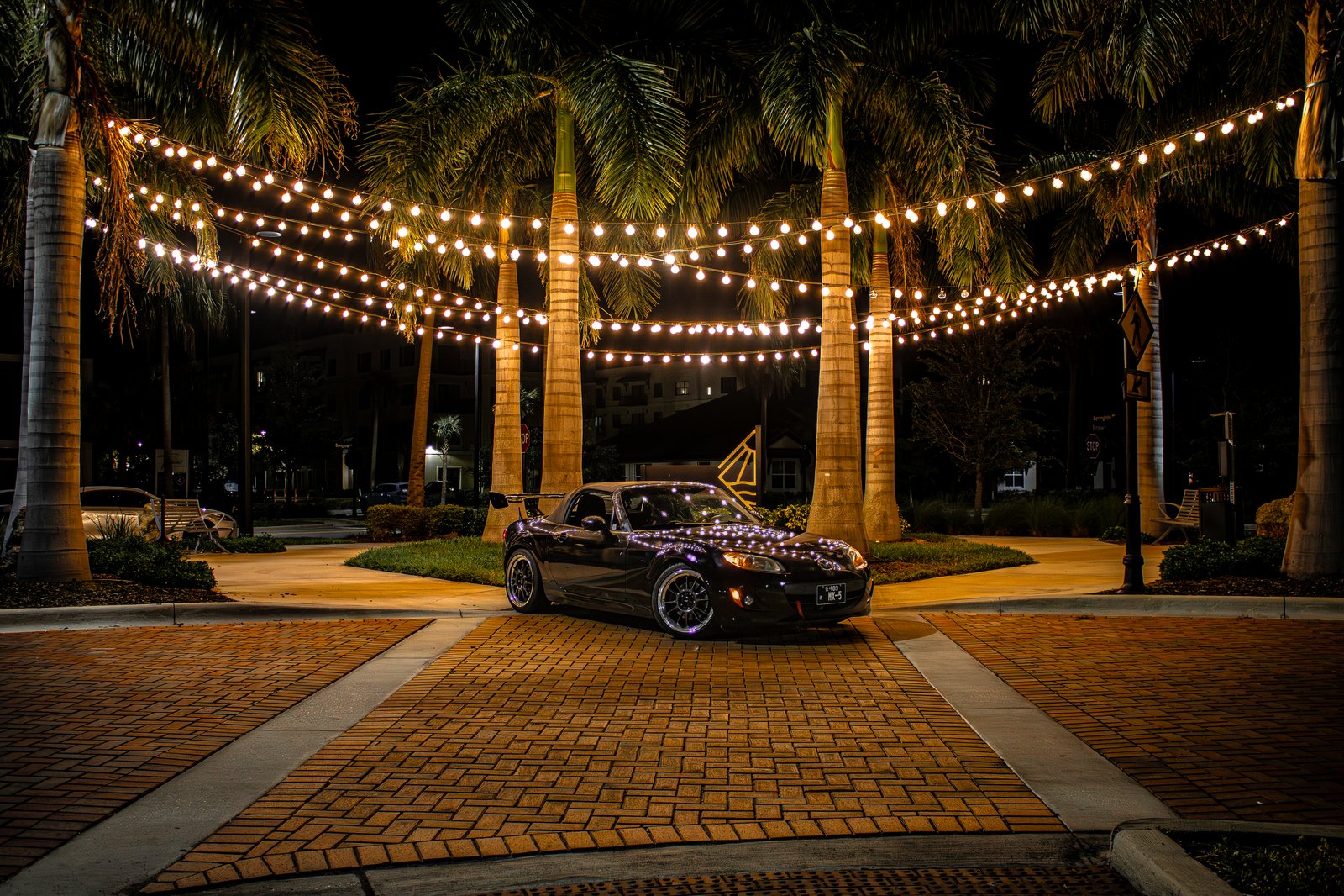 Black Mazda MX-5 Miata under palm tree string lights at night — automotive photography by Flicks With Ale in Southwest Florida